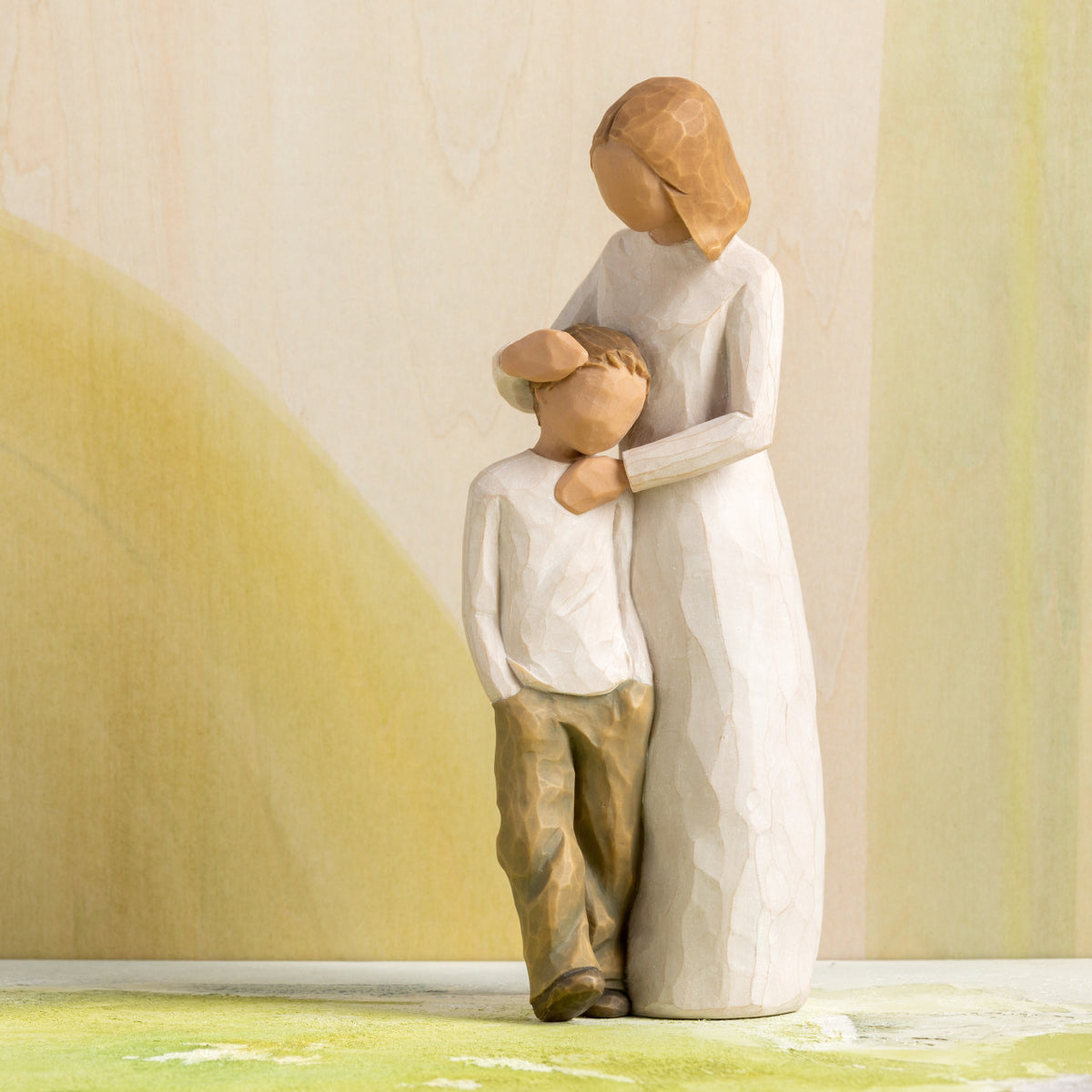 Willow Tree Mother and Son, 8”h hand-painted standing resin figure with arms around young boy, both in neutral clothing, in front of ochre painting