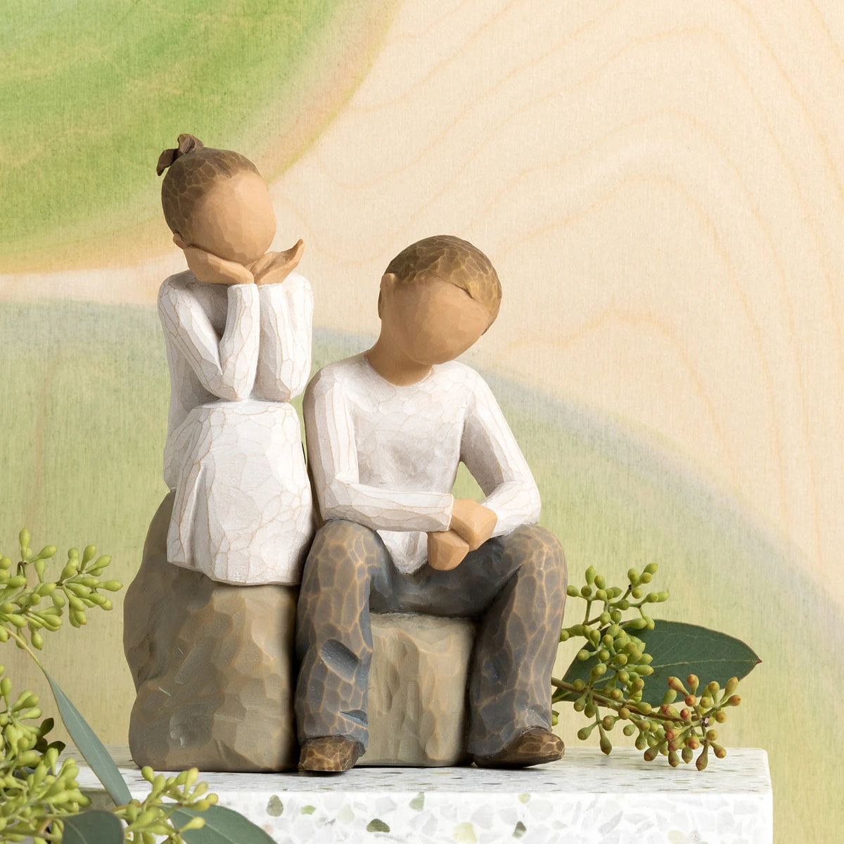 Willow Tree Brother and Sister, 5.5”h hand-painted resin figure of boy and girl, seated together on gray rock, both in neutral clothing, in front of pale green painting