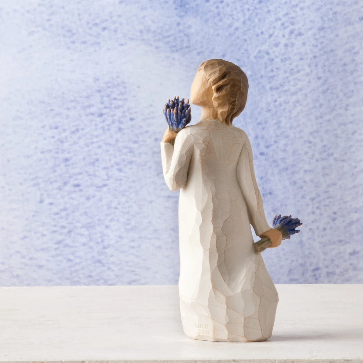 Small girl figurine wearing white dress holding two blue flower bouquets in each hand