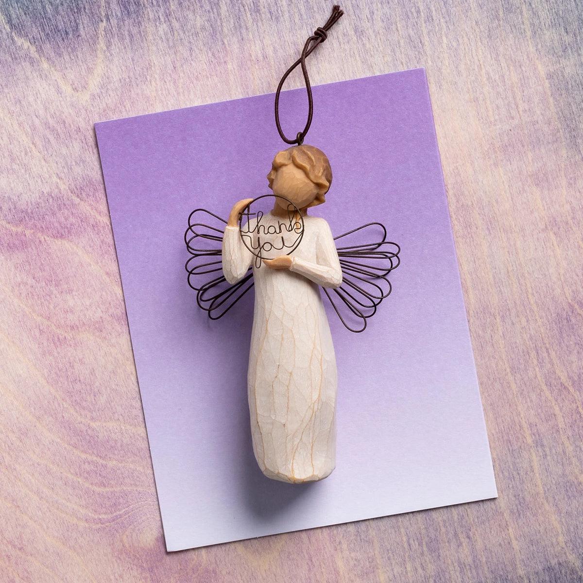 Willow Tree Just for You Ornament, 4”h hand-painted resin angel ornament in cream dress with wire wings, holding wire circle with 'thank you' written in wire, laying on lavender painting