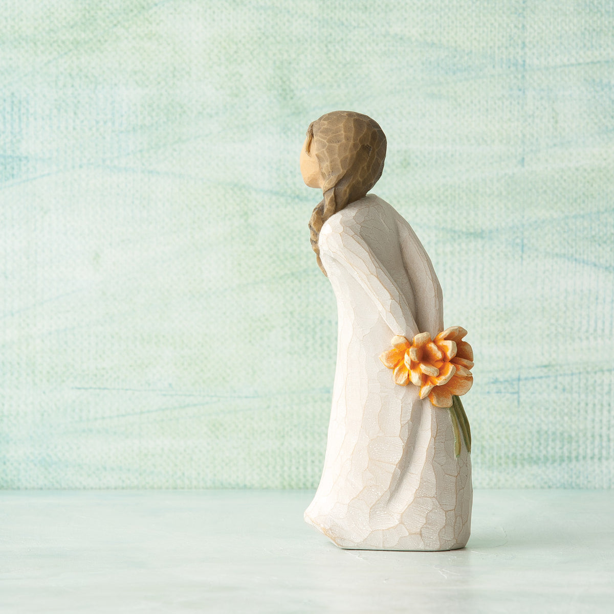 Willow Tree For You, 5”h hand-painted standing resin figure in cream dress, holding bouquet of orange flowers behind back, in front of pale green painting