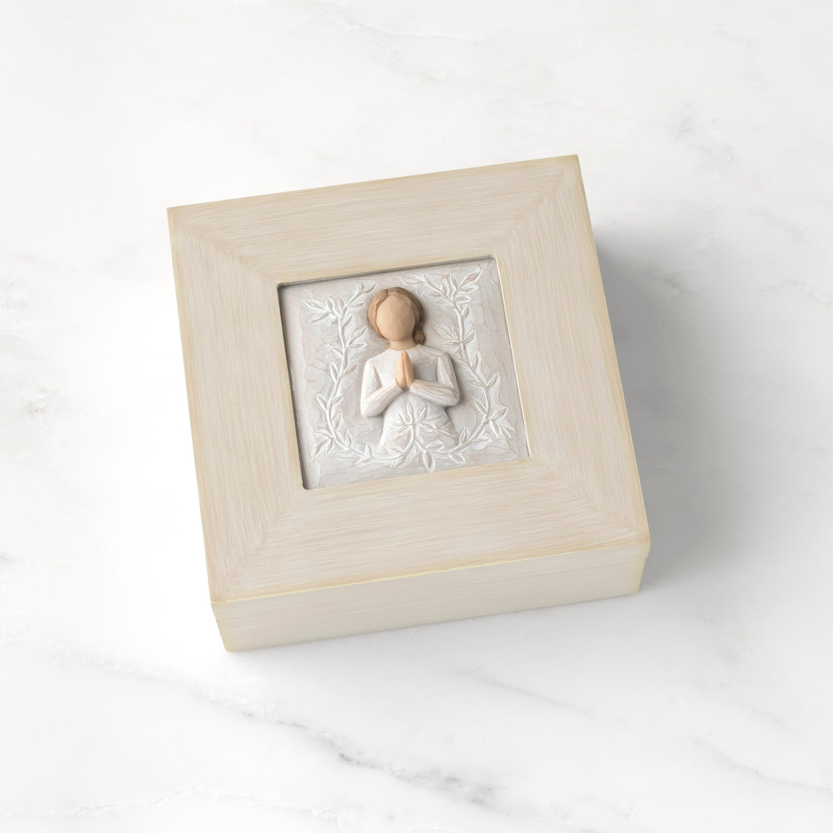 Cream square wood box with hinged lid, carving on lid of female in cream dress with hands in prayer position, surrounded by leaves and vines
