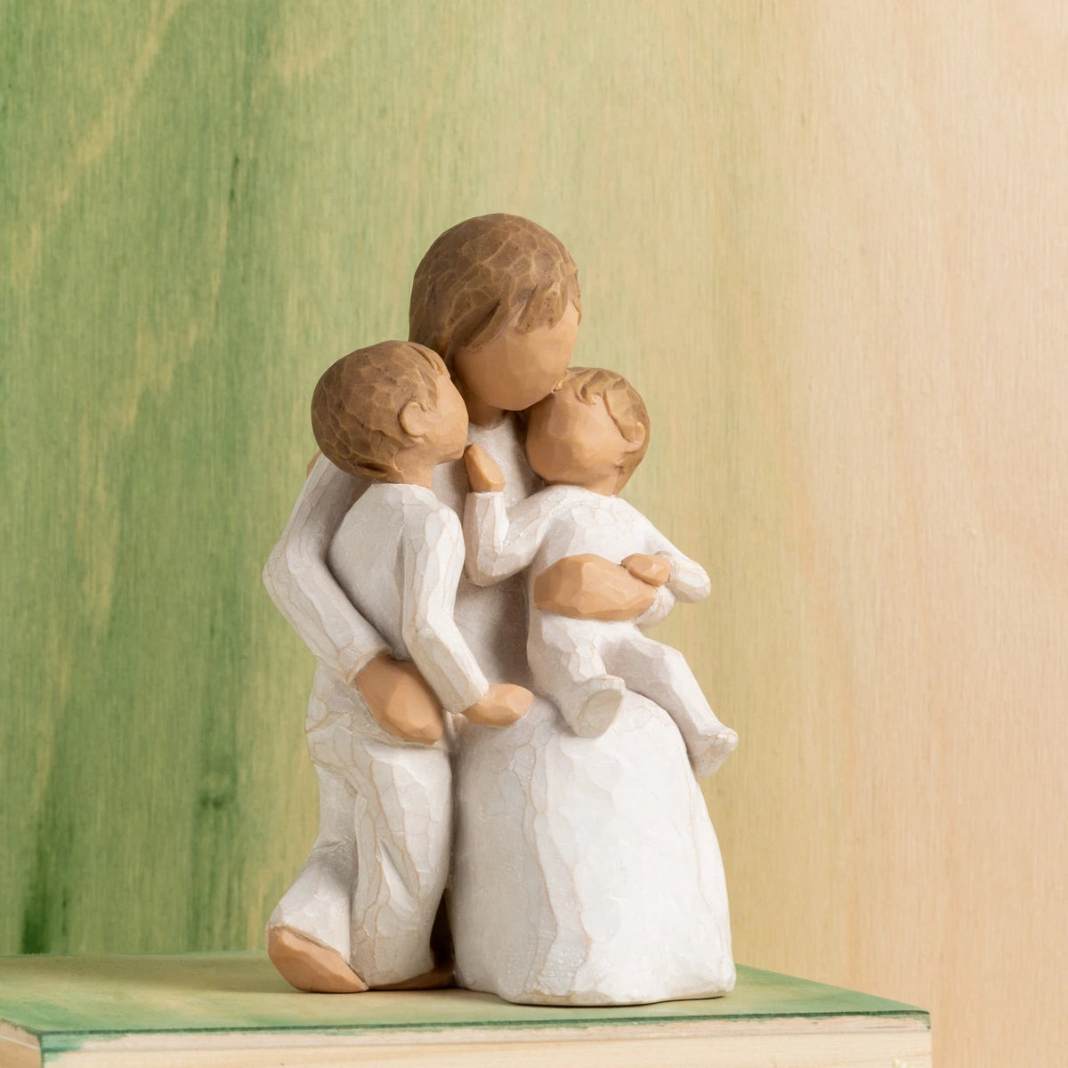 Willow Tree Quietly, 5”h hand-painted seated resin figure, one arm holding small toddler, other arm around standing older child, all in cream clothing, in front of green painting