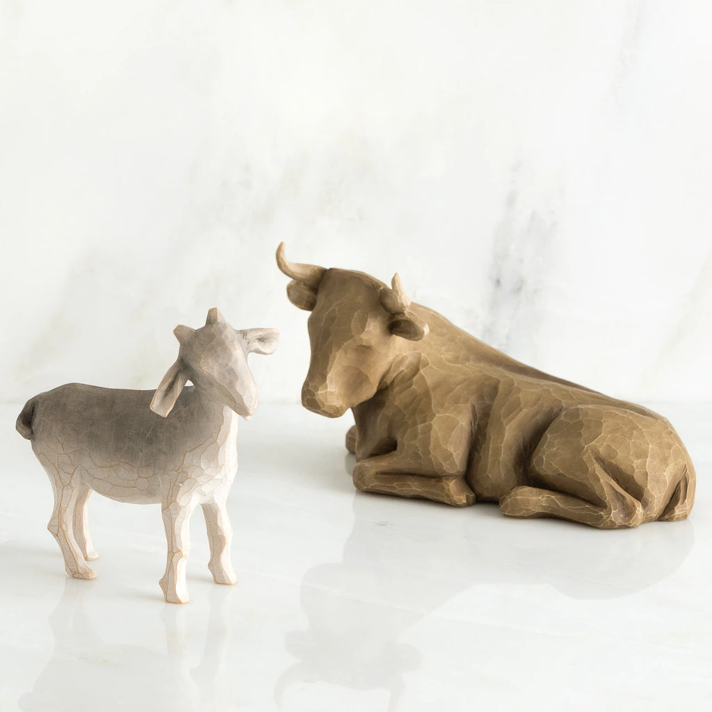 Brown cow figurine laying next to white goat figurine standing up