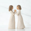 Two brunette girl figurines in white dresses holding hands facing one another