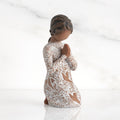 Front: Kneeling figure with darker skin, hands in position of prayer or meditation in cream dress carved with icons of nature