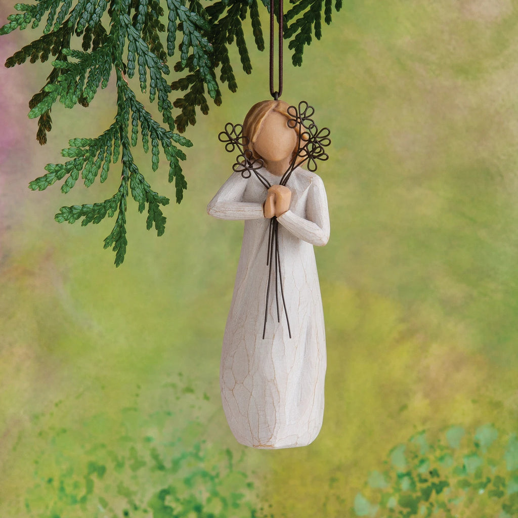 Willow Tree Friendship Ornament, 5.5"h hand-painted resin figure in cream dress holding wire flowers with long stems, brown elastic cord, hanging in front of mossy green painting