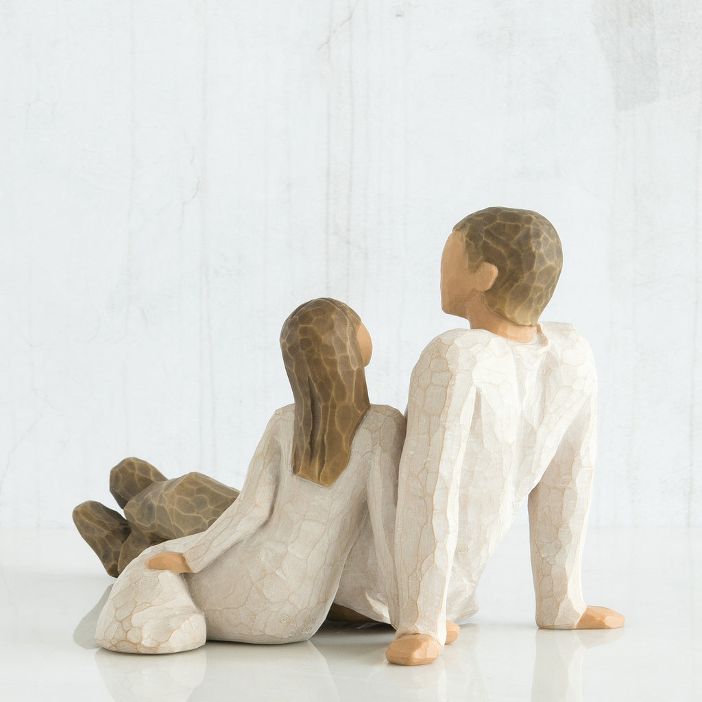 Back view of father figurine sitting next to daughter figurine - both wearing white