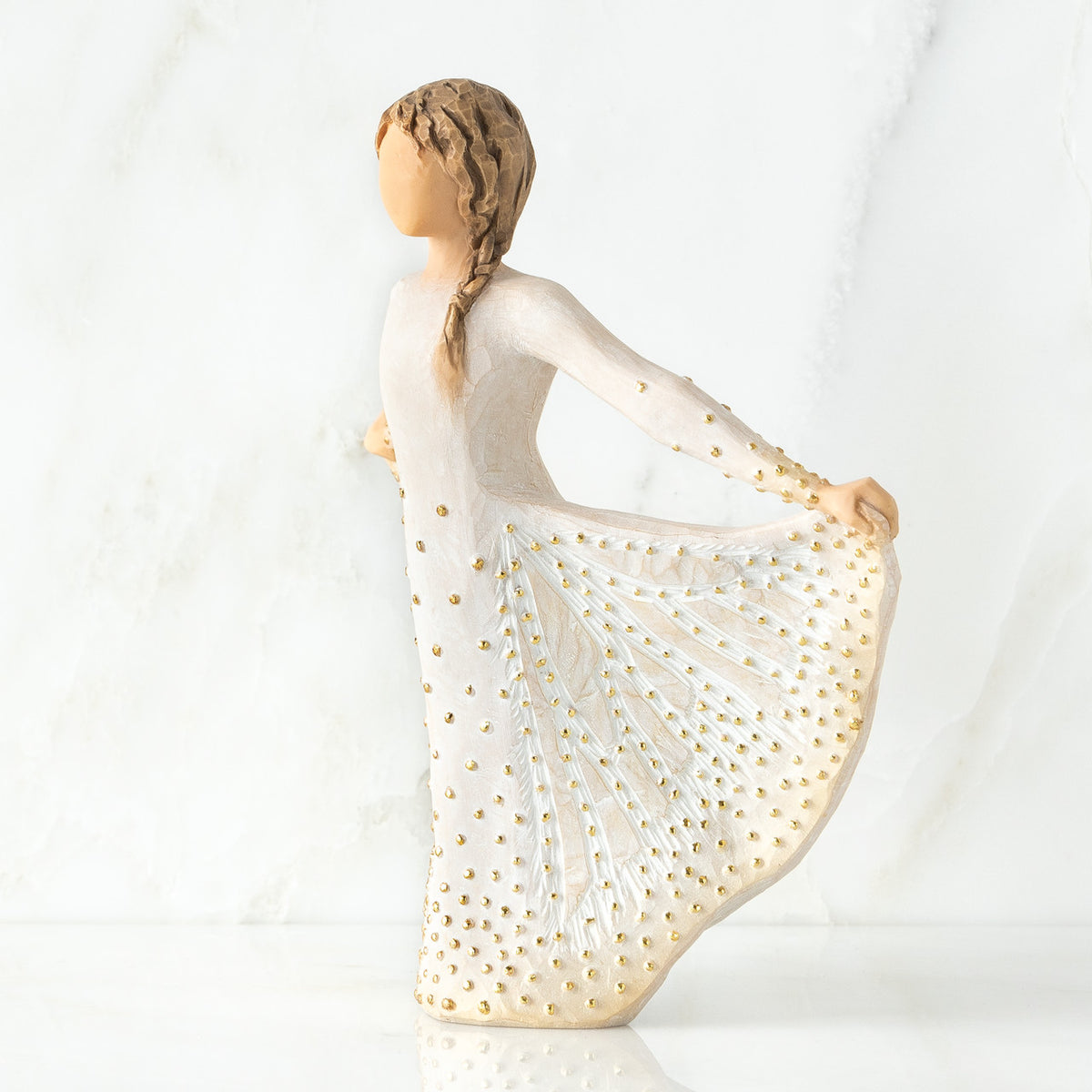 Left view of standing female figure in cream dress, holding out her skirt, which is carved with butterfly markings and dotted with gold