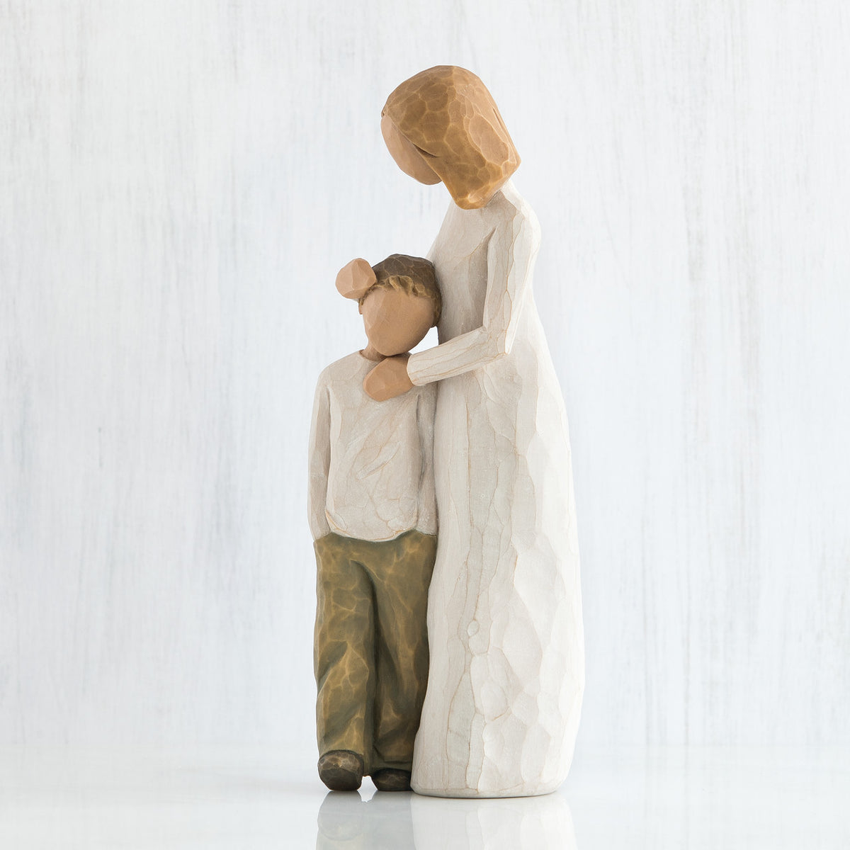 Side view of blonde mother figurine in white with hands on younger boy figurine in brown pants and white shirt