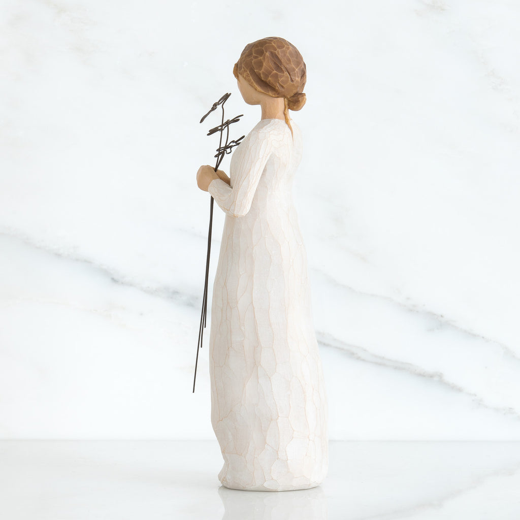 Right side view of girl with brown hair in a bun holding three flowers with long stems up to her chest with both hands