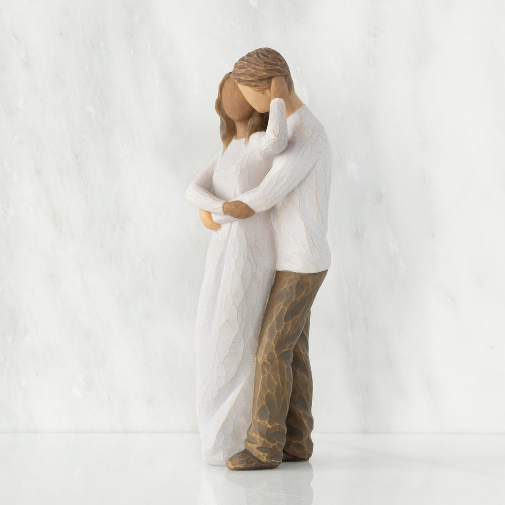 Left view of couple, standing with arms around each other. Woman has darker skin and hair; man has lighter skin and hair.