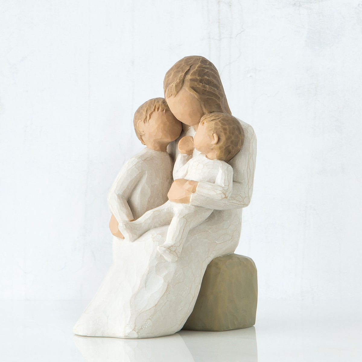 Mother figurine in white dress sitting on rock holing her two baby figurines in her lap