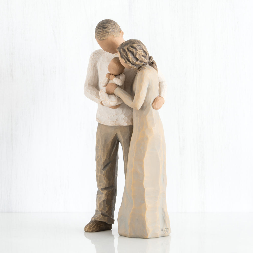 Close view of man and woman figurine holding baby in their arms - wearing brown colors