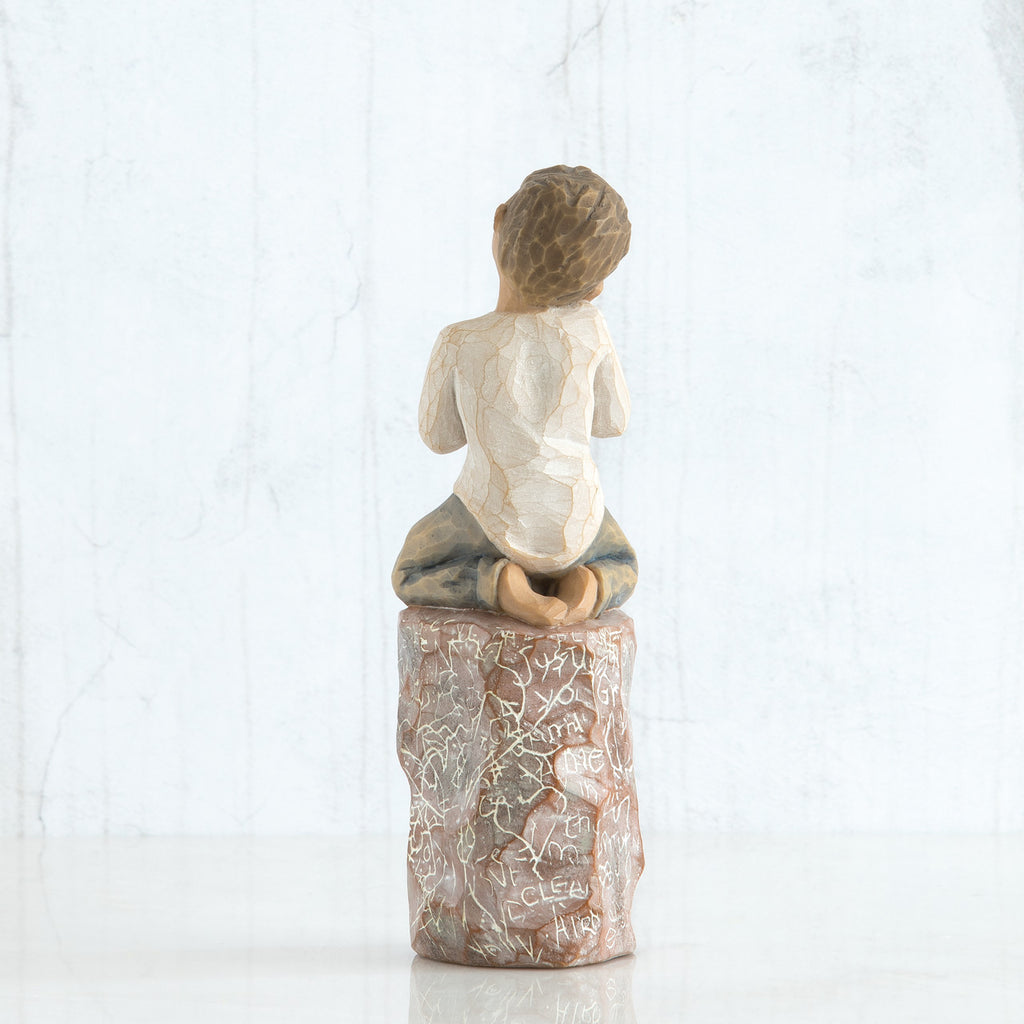 Back view of boy with brown hair sitting on a stump while holding a small potted plant to his chest