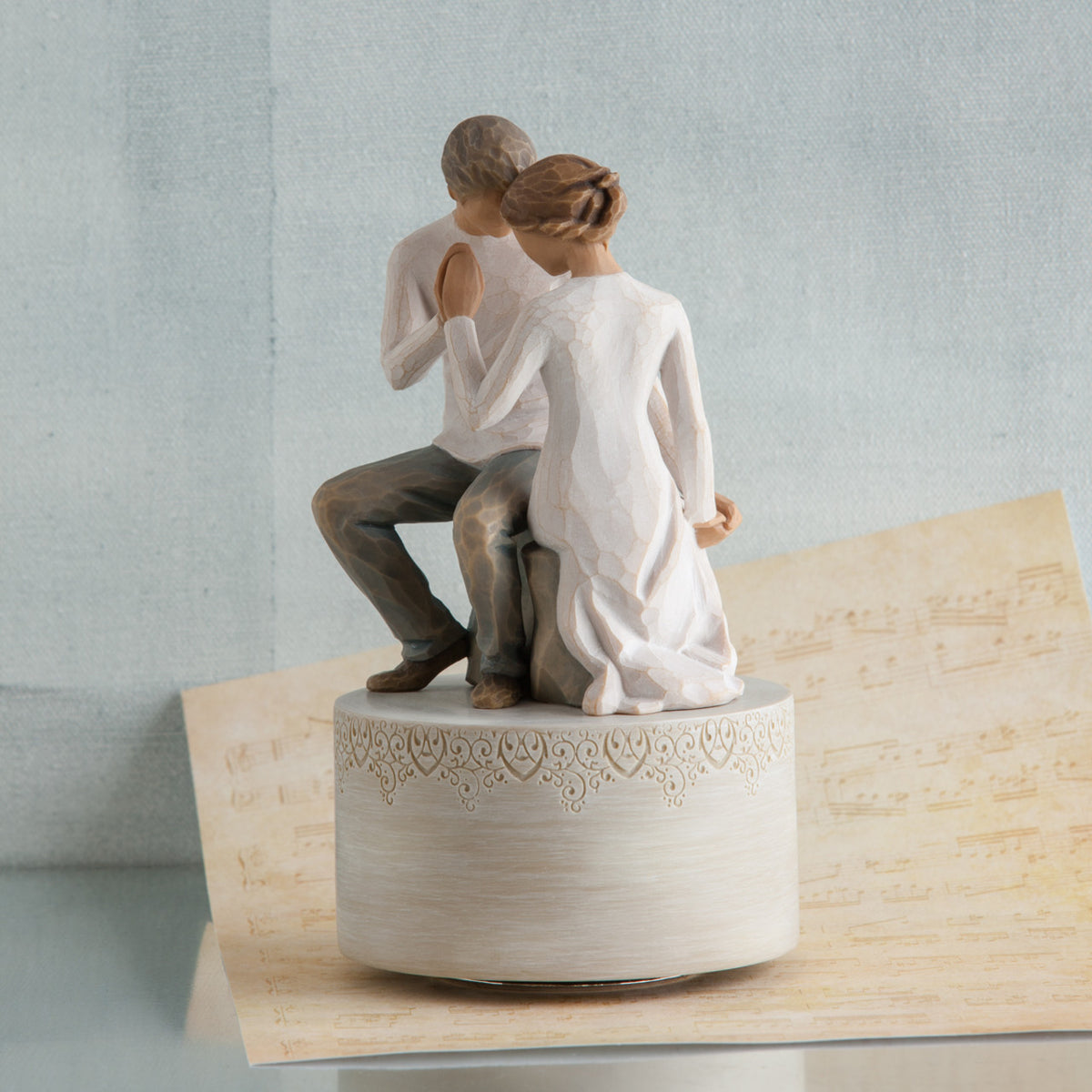 Couple figurine sitting holding hands on white round plaque