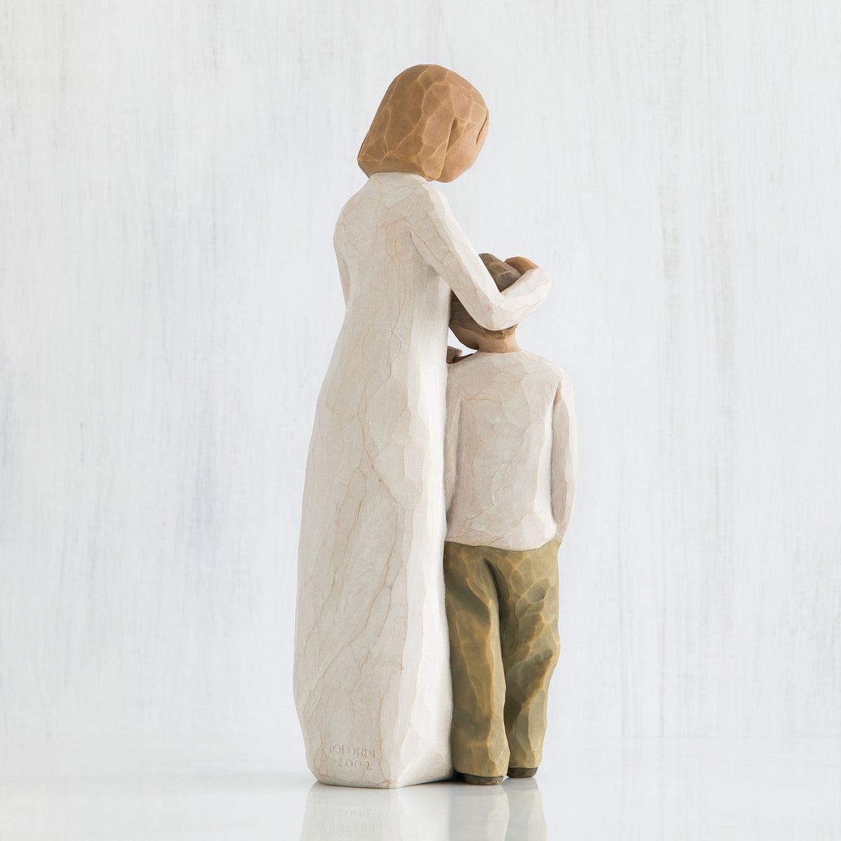 Blonde woman figurine in white dress with arms over boy figurine in white shirt and brown pants