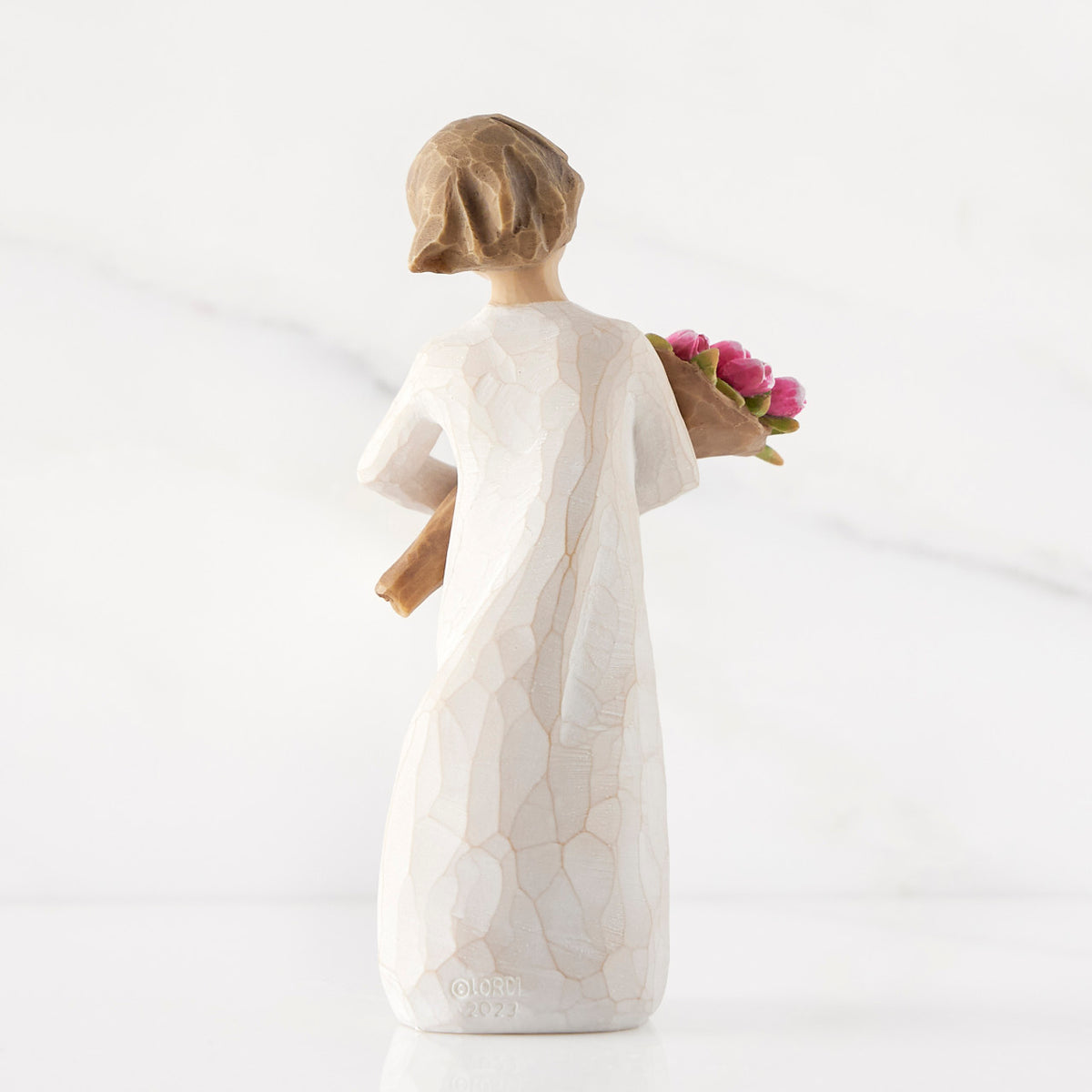 Back view of standing figure in cream dress holding bouquet of pink tulips