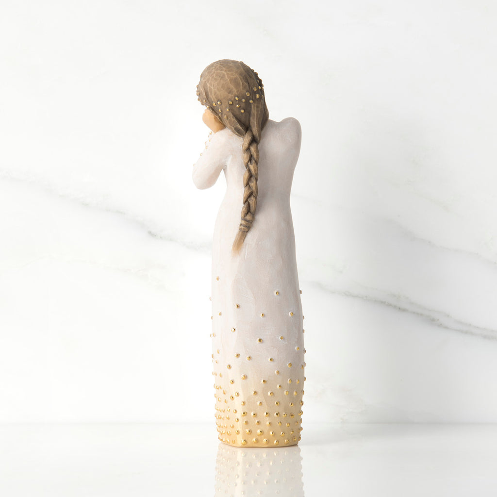 Back view, standing figure in cream dress, showing long braid, and gold-leaf dot detail on dress and hair