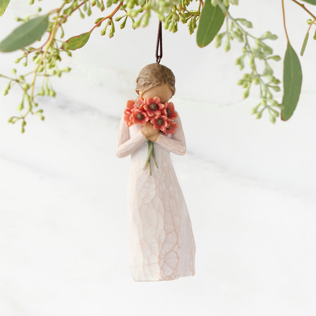 Figure in cream dress holding large bouquet of red-orange poppies up to face, ornament hook attached to head