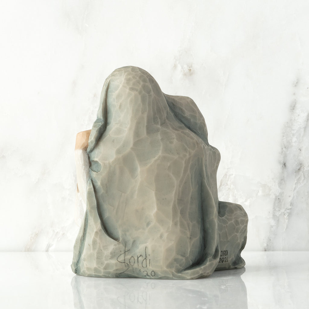 Back view: seated figure with arms around two younger figures, all wrapped in a blue-gray blanket