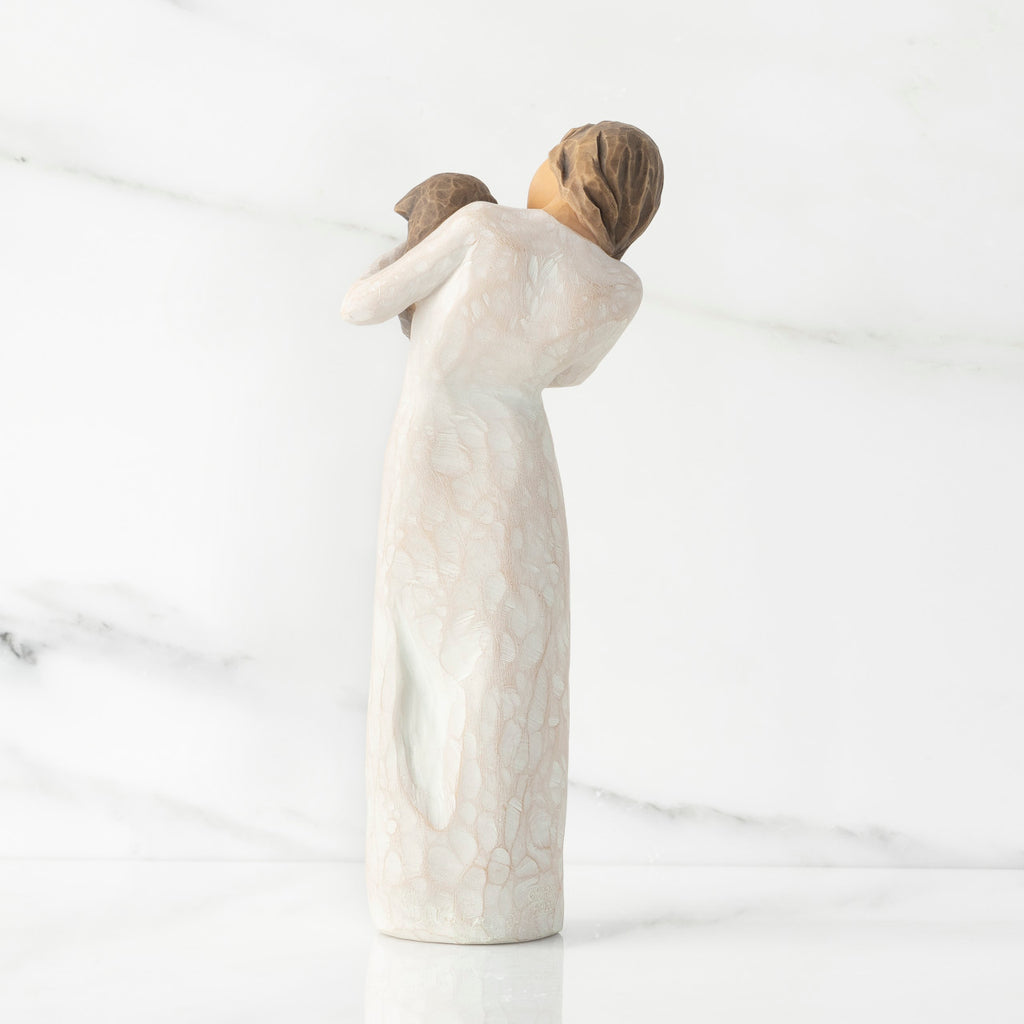 Back view, standing female figure in cream dress, holding dark color puppy in her arms