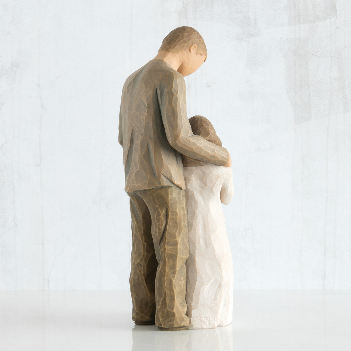 Back view of man figurine in brown looking down at younger daughter in white with arm around her