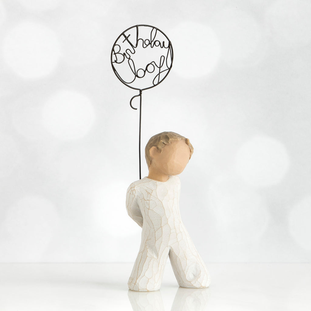 Front view of little boy with light brown hair holding a wire balloon behind his back. Text on balloon is wire