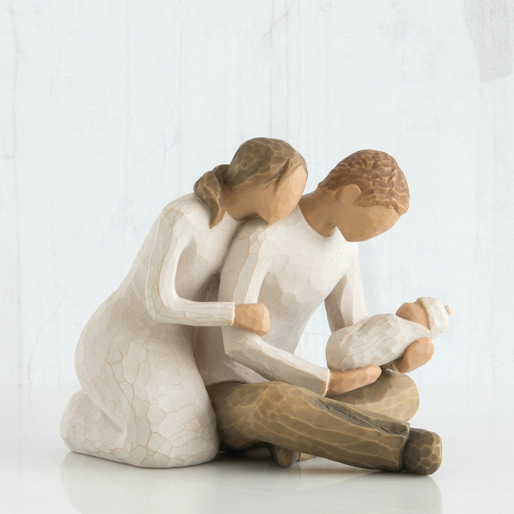 Faceless woman figurine in white dress leaning on faceless man figurine holding baby in his lap
