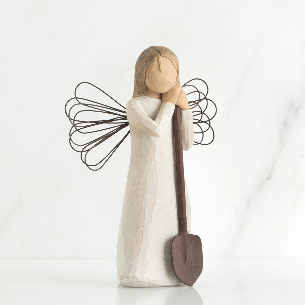 Young faceless girl figurine in white dress with black wire wings holding brown shovel