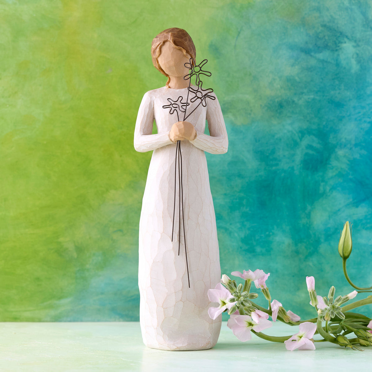 Willow Tree Grateful, 9”h hand-painted standing resin figure in cream dress, holding three wire flowers with long stems, in front of deep teal painting