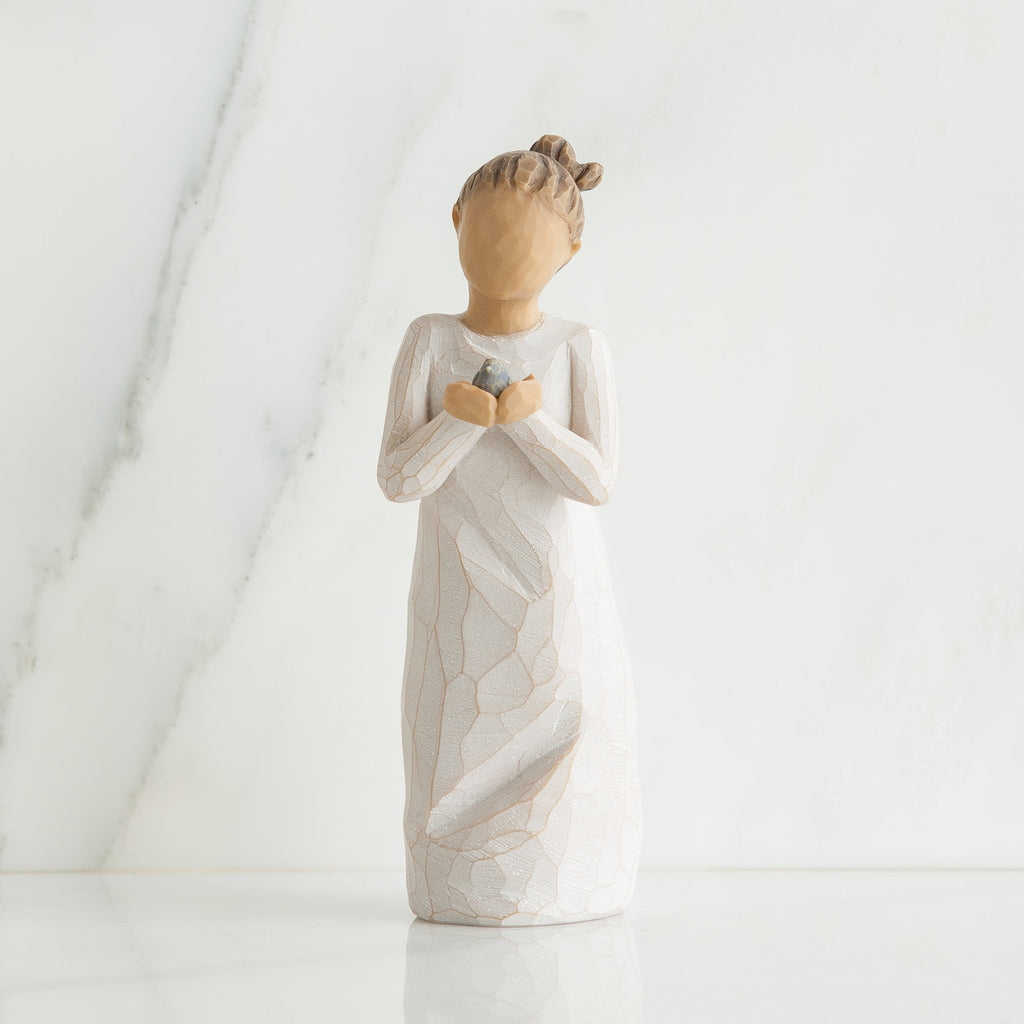 Front view of woman with brown hair in a high ponytail leans forward as she holds a gray bird to her chest with both hands