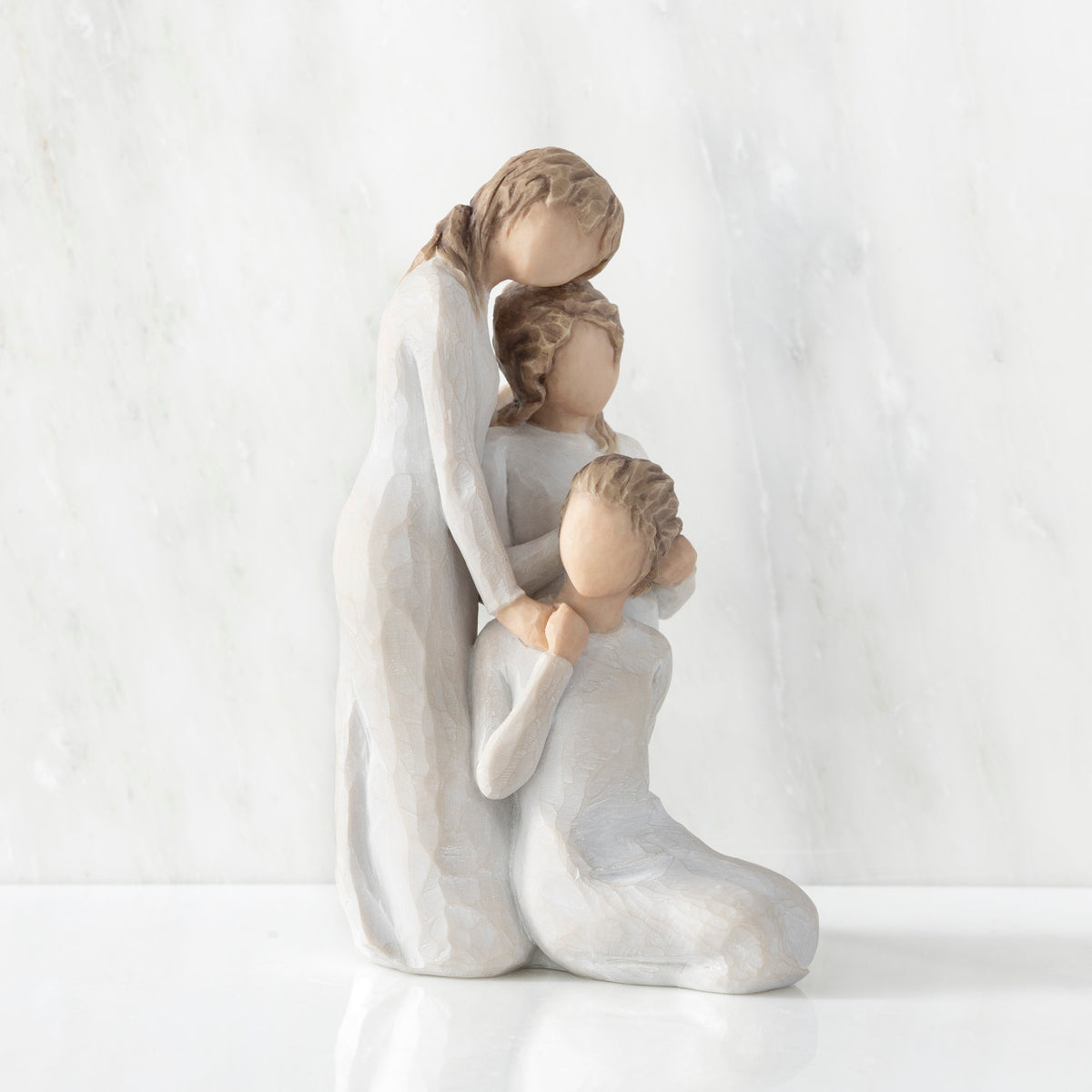 Right-facing view, figurine of three females in cream dresses: one standing with arm around kneeling female, and holding hand of seated female