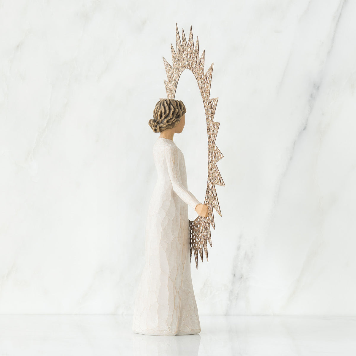 Brunette woman figurine wearing white dress facing away from the camera holding rose gold sun figurine up