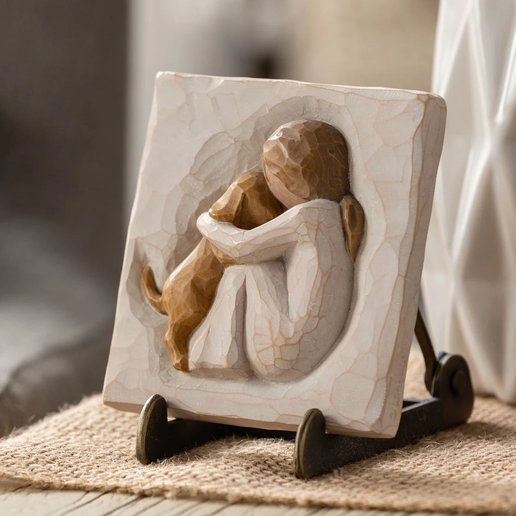 Willow Tree True Plaque, 4”sq x .5”d hand-painted resin bas-relief carving of seated figure in cream dress, golden puppy climbing onto lap, Plaque displayed on Plaque Stand on table