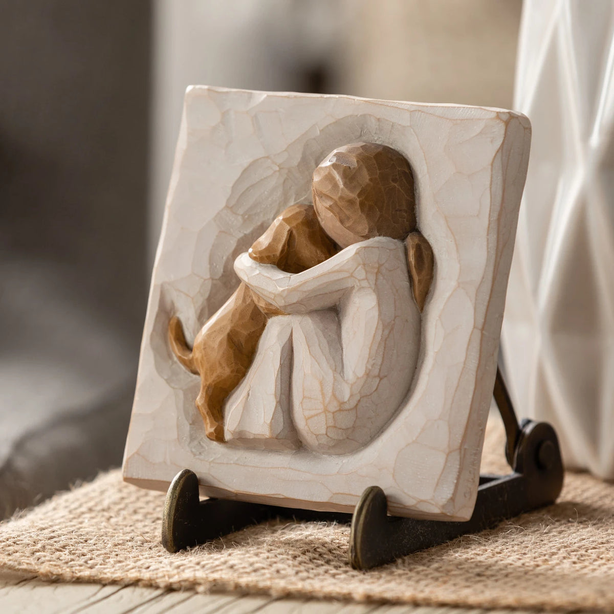 Willow Tree True Plaque, 4”sq x .5”d hand-painted resin bas-relief carving of seated figure in cream dress, golden puppy climbing onto lap, Plaque displayed on Plaque Stand on table