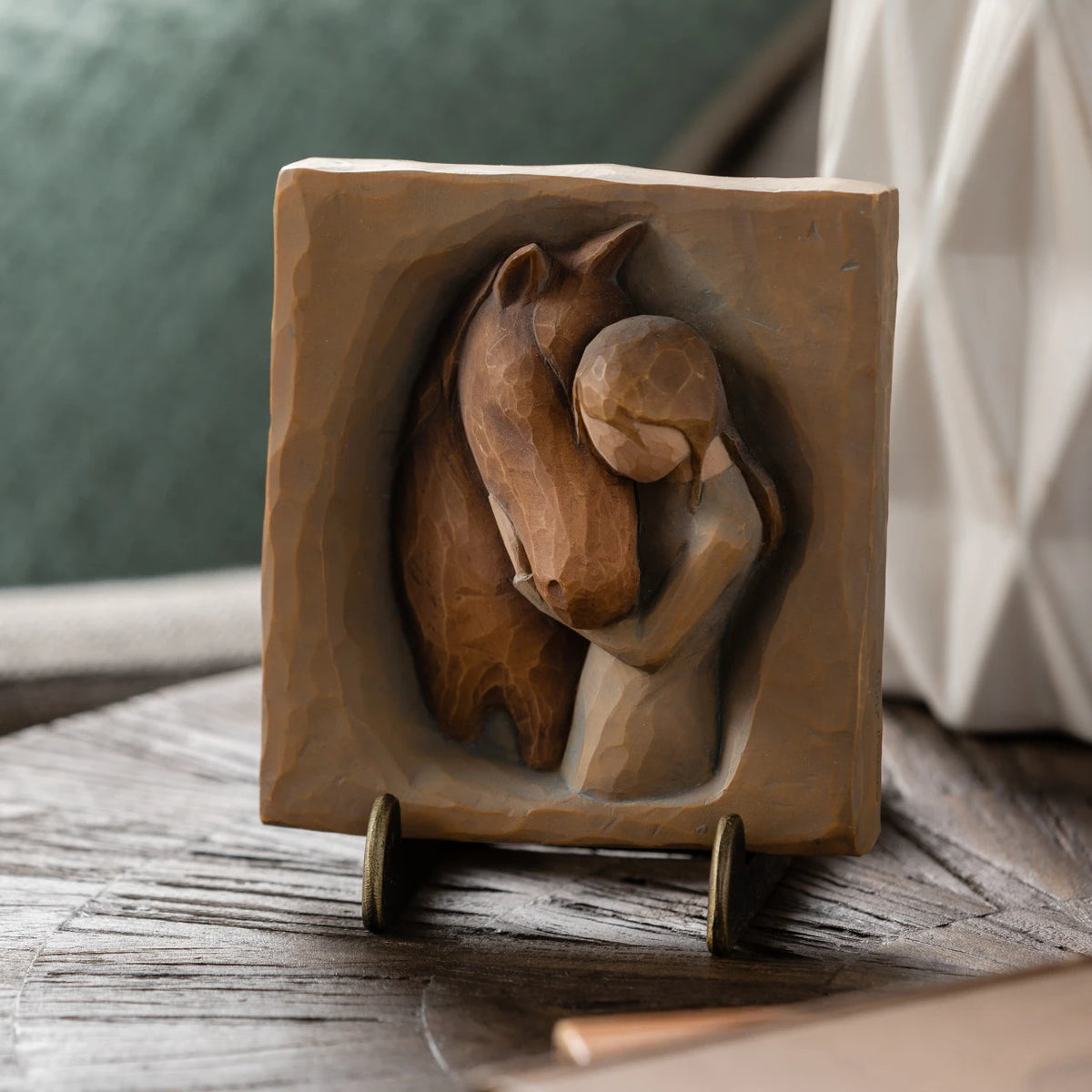 Willow Tree Hug Plaque, 4”sq x .5”d hand-painted resin bas-relief carving of girl in cream dress, arms around neck of reddish-color horse, on green/gray background. Plaque displayed on Plaque Stand on table