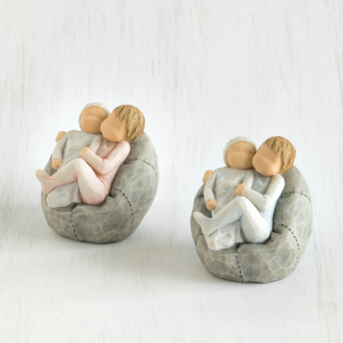 Set of two - baby figurines being held by larger sibling figurines on grey bean bags