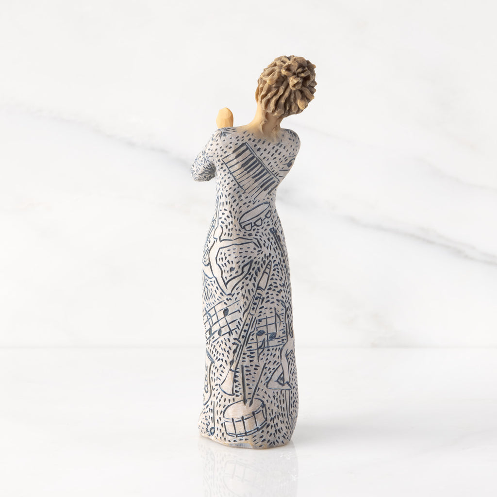 Back view: Lighter-skin figure carved with contrasting pattern of dark blue musical symbols, instruments, dancing forms