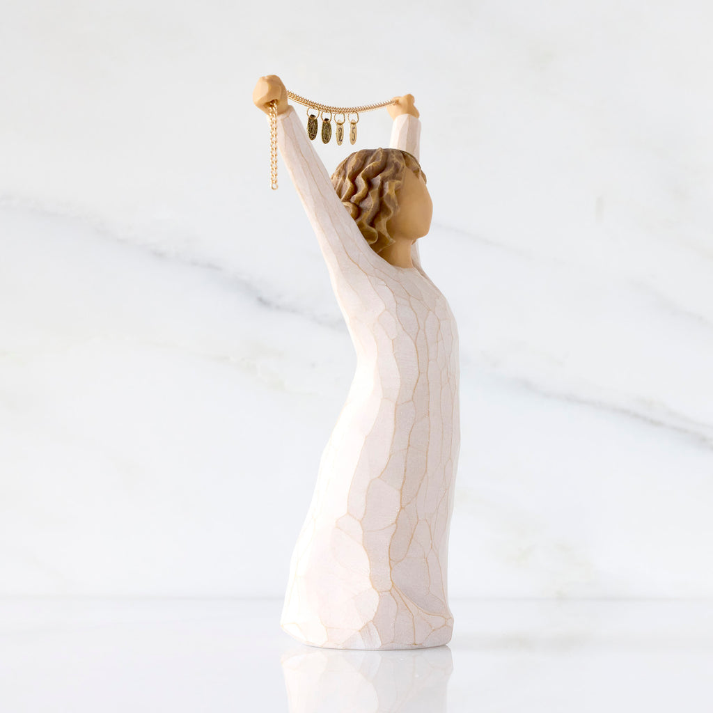 Willow Tree Courage 2025, side view of 6”h hand-painted standing figure in cream dress holding aloft a gold chain with 2025 etched on gold medallions