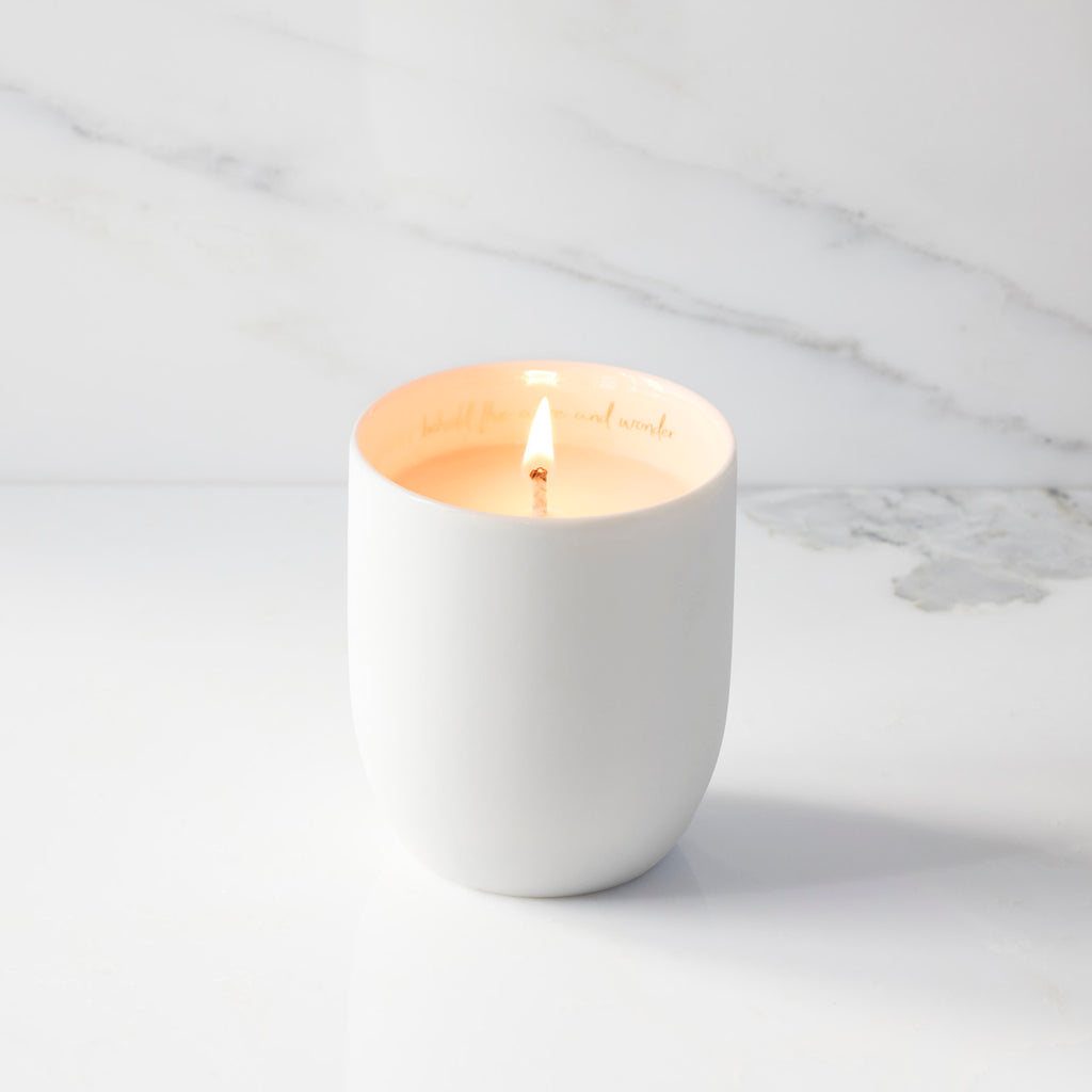 Lit filled scented candle with unglazed cream tapered cylinder vessel, sentiment written in gold inside rim, plant-based wax blend, all-cotton wick