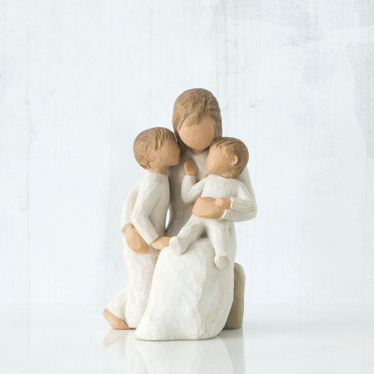 Faceless mother figurine sitting down holding two faceless children figurines in her arms