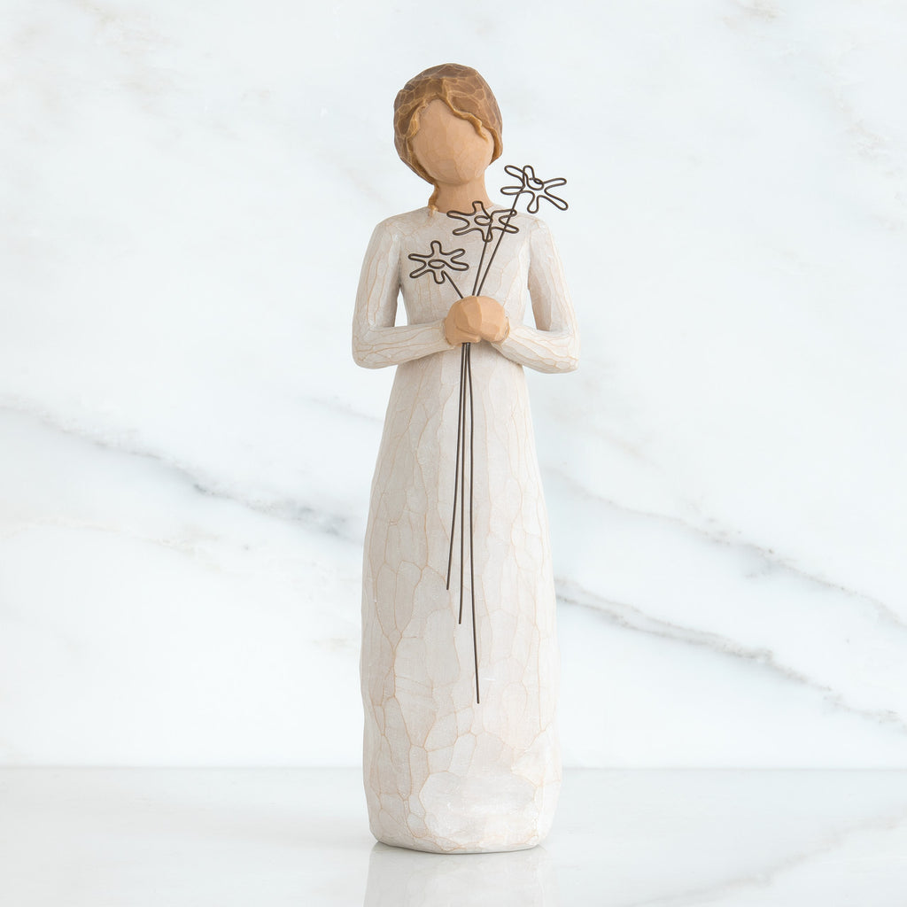 Front view of girl with brown hair in a bun holding three flowers with long stems up to her chest with both hands