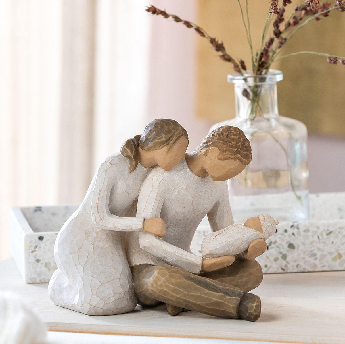 Willow Tree New Life, 5”h hand-painted resin figure of seated couple in neutral colors, holding newborn baby wrapped in cream blanket, on bedroom dresser