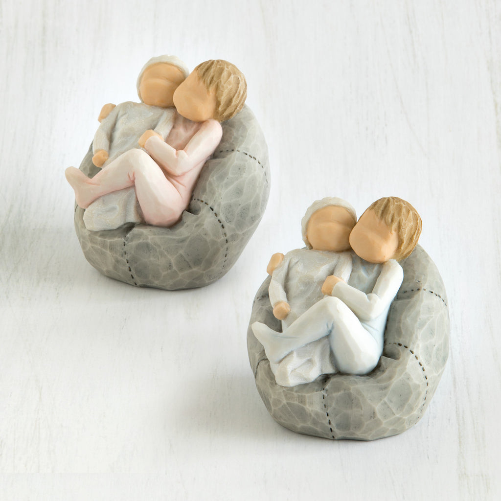 Set of two baby figurines on grey beanbags being held by their older sibling