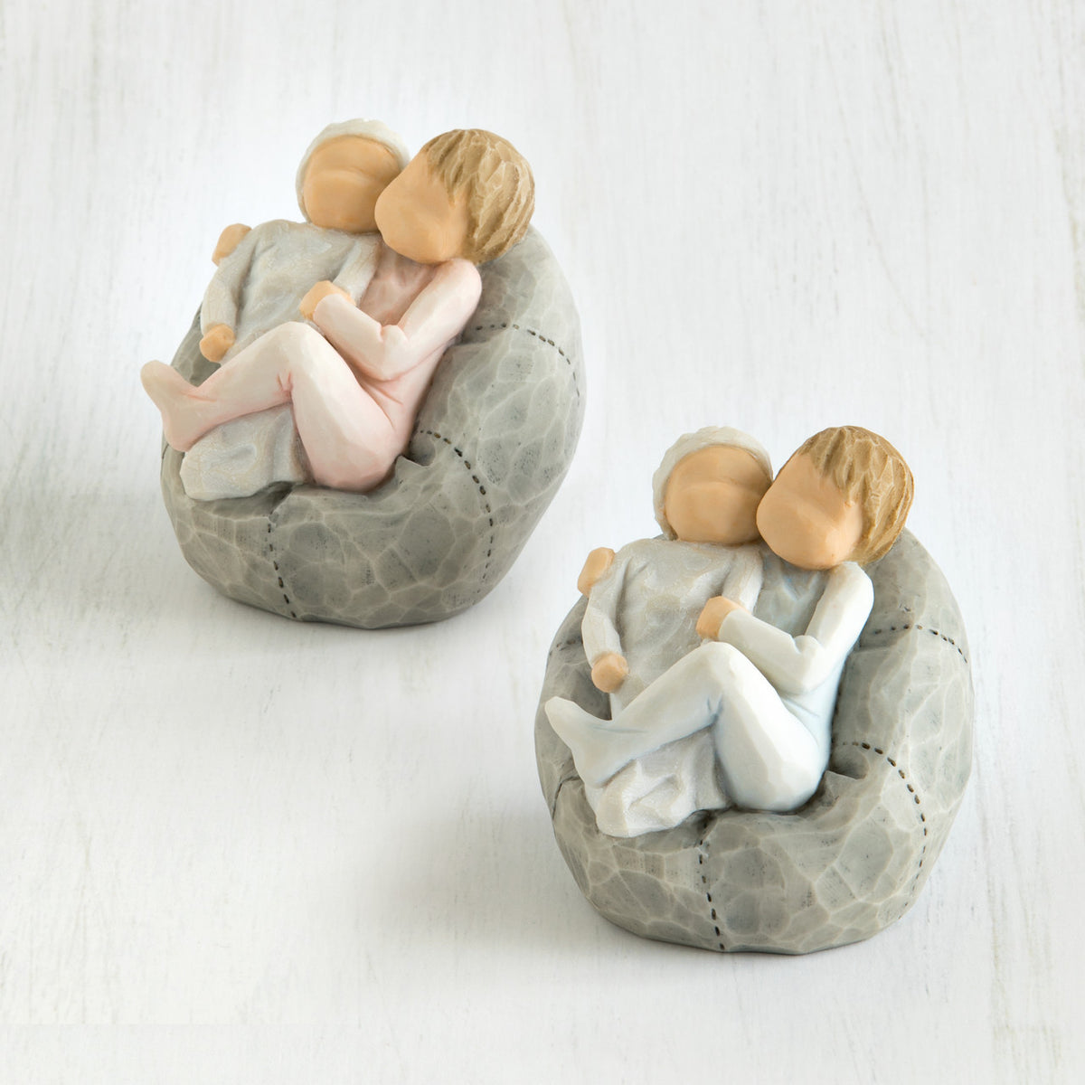 Set of two baby figurines on grey beanbags being held by their older sibling
