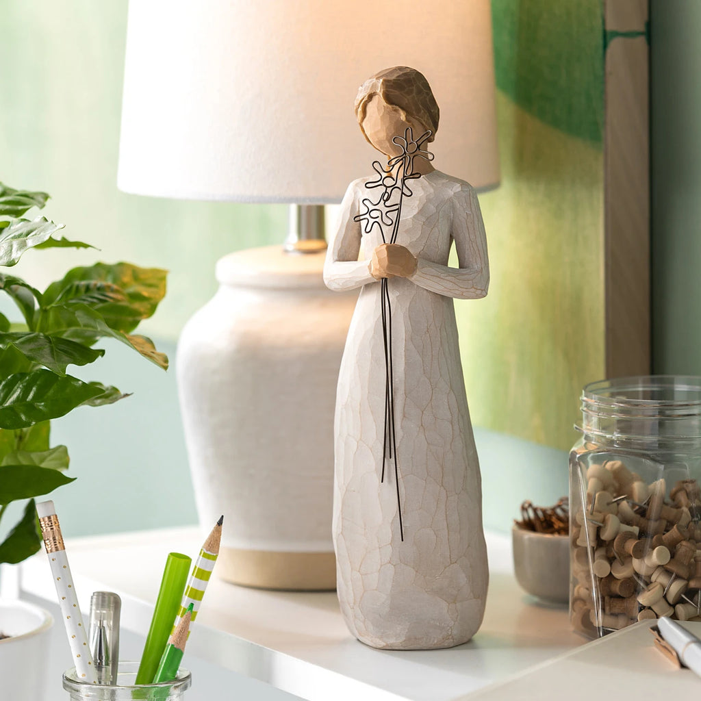 Willow Tree Grateful, 9”h hand-painted standing resin figure in cream dress, holding three wire flowers with long stems, on shelf with white lamp