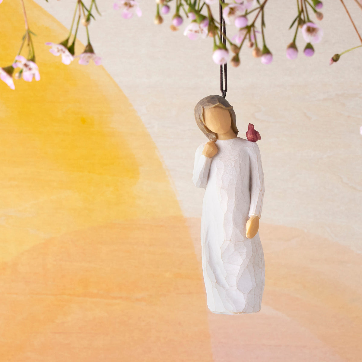 Willow Tree Messenger Ornament, 4”h hand-painted resin figure in cream dress with red cardinal on shoulder, brown elastic cord, hanging in front of orange painting
