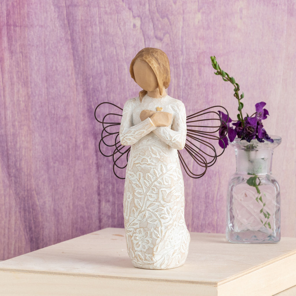 Willow Tree Remembrance, 5”h hand-painted standing resin angel figure in cream dress carved with symbols of nature, wire wings, crossed hands under small gold-leaf heart, in front of purple painting