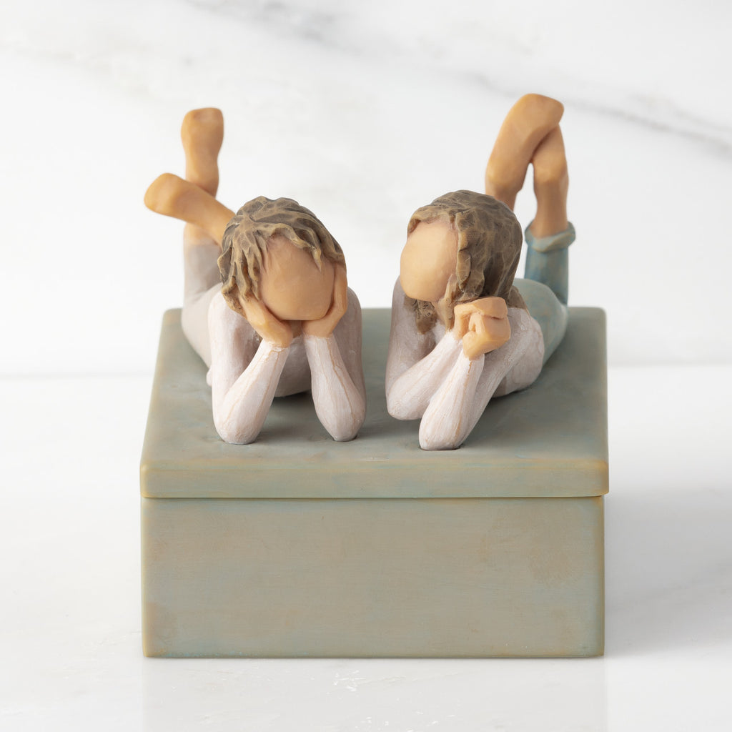 Front view of closed rectangular blue-gray resin box, sculpture of two girls affixed to lid
